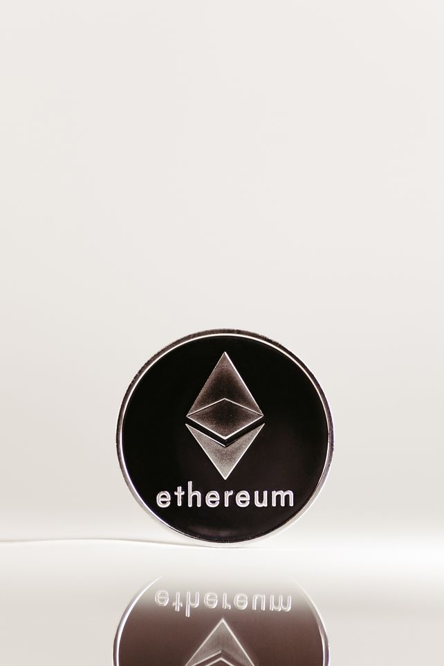Close-up of an Ethereum cryptocurrency coin with a minimalist design on a reflective surface.
