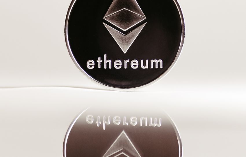 Close-up of an Ethereum cryptocurrency coin with a minimalist design on a reflective surface.