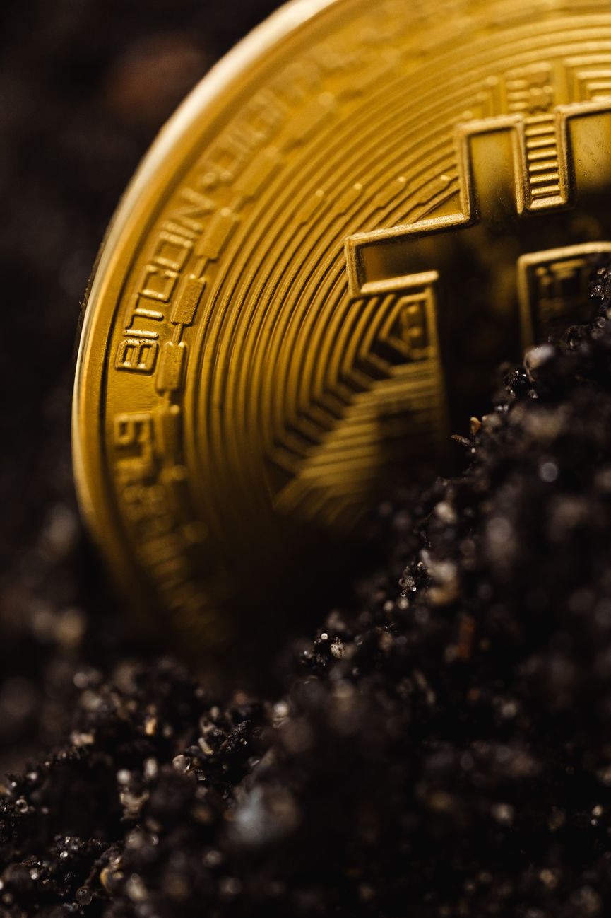 Detailed close-up of a gold Bitcoin partially buried in dark soil, symbolizing digital wealth.