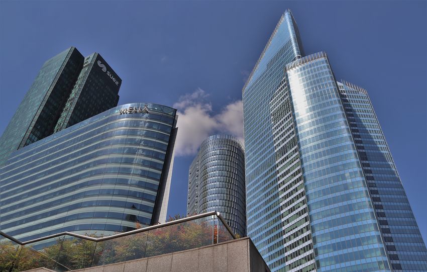 Dynamic low angle view of glass skyscrapers in La Défense, Paris under a clear blue sky.