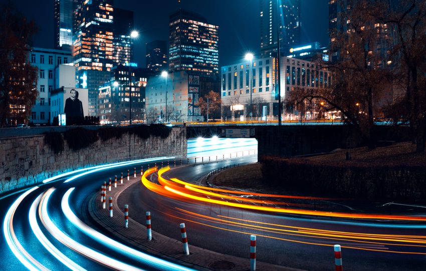 Long exposure of dynamic traffic lights against Warsaw's illuminated skyline at night.