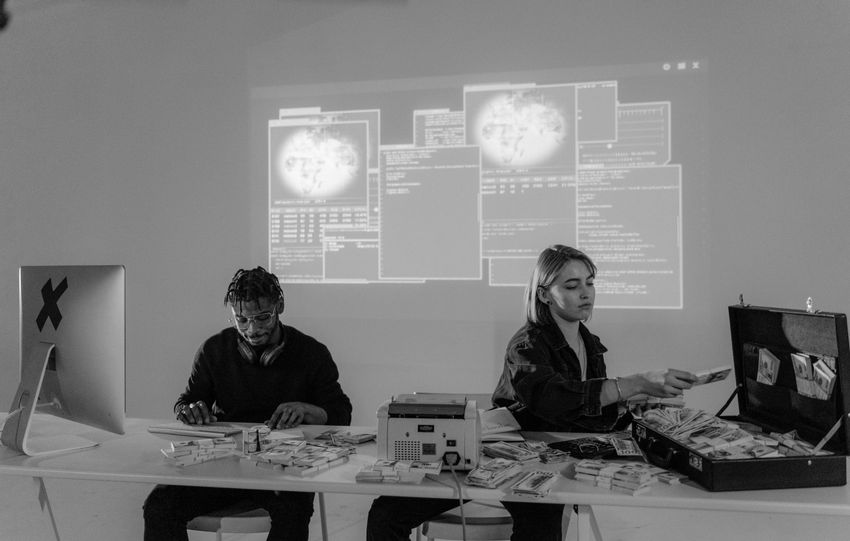 Two professionals in a high-tech environment working with cash and computers, analyzing complex data.